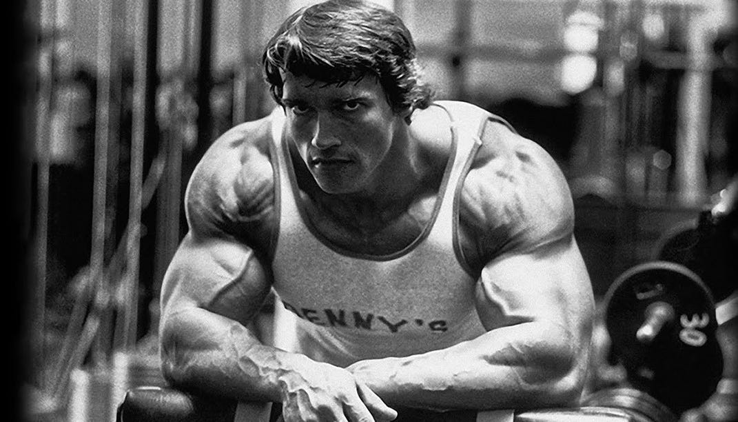 Black and white image of Arnold Schwarzenegger, a symbol of determination in fitness, highlighting the importance of a custom gym nutrition strategy. Check https://karanblog.in/.