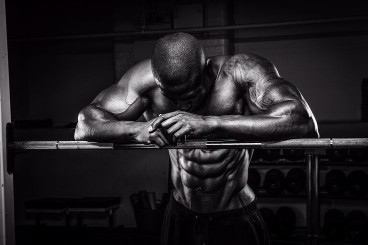 Highly defined, personalized muscle of a male bodybuilder resting on a barbell in a black and white gym setting, perfect for fitness motivation. Visit https://karanblog.in/ for more.