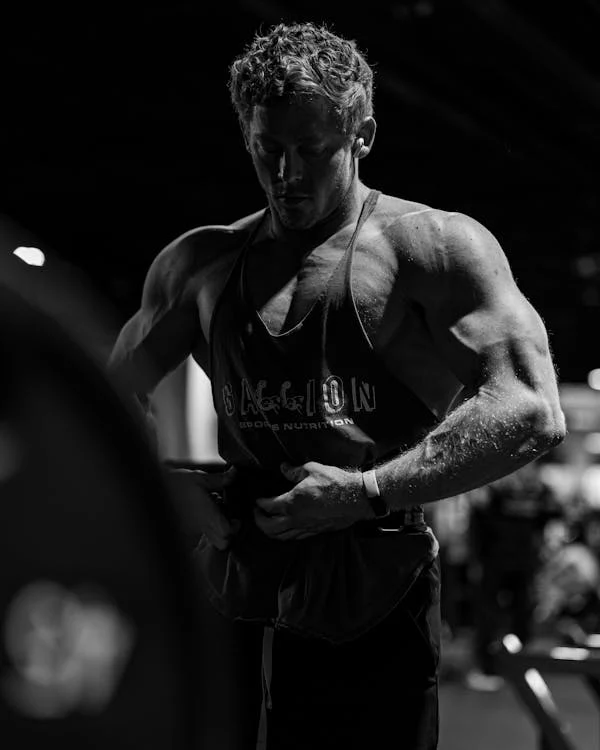 A male fitness enthusiast with visible muscle definition, reflecting on his progress in a gym, highlighting the results of a custom gym nutrition strategy. Visit https://karanblog.in/.