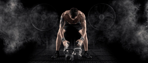 Sporty man with kettlebells on a dark, smoky gym floor, representing focus and the essential role of healthy eating in fitness. Check out https://karanblog.in/.